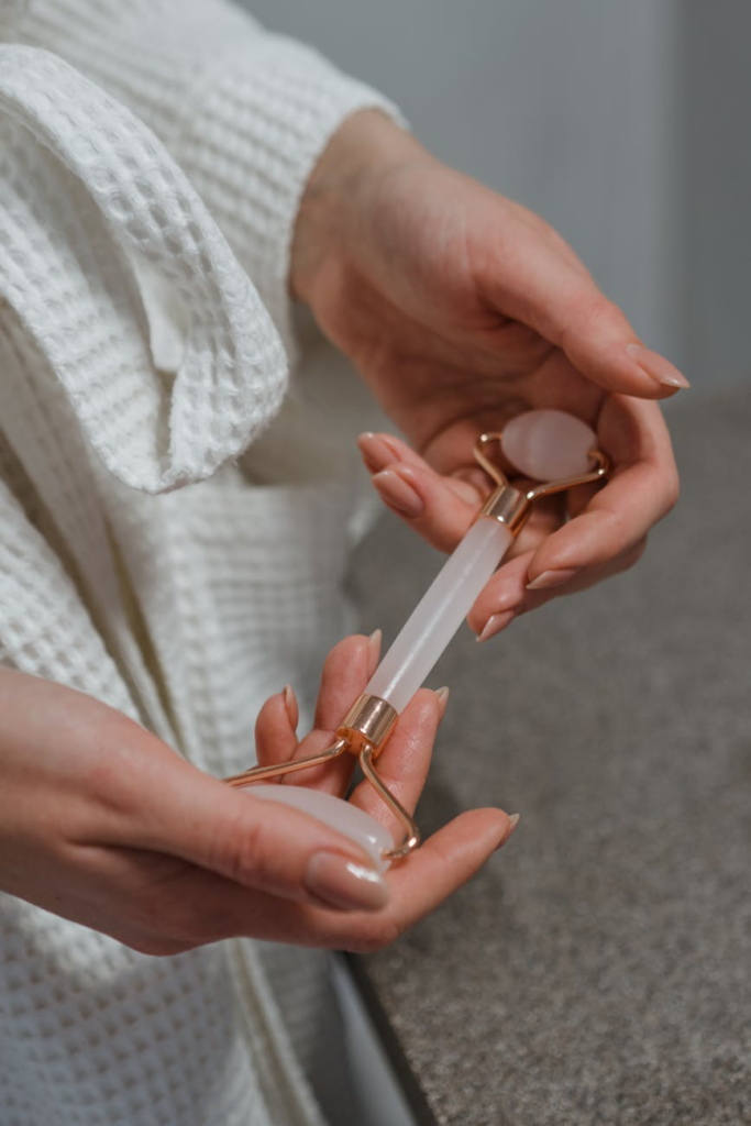 Close-up of hands holding a rose quartz facial roller in a relaxing spa environment.